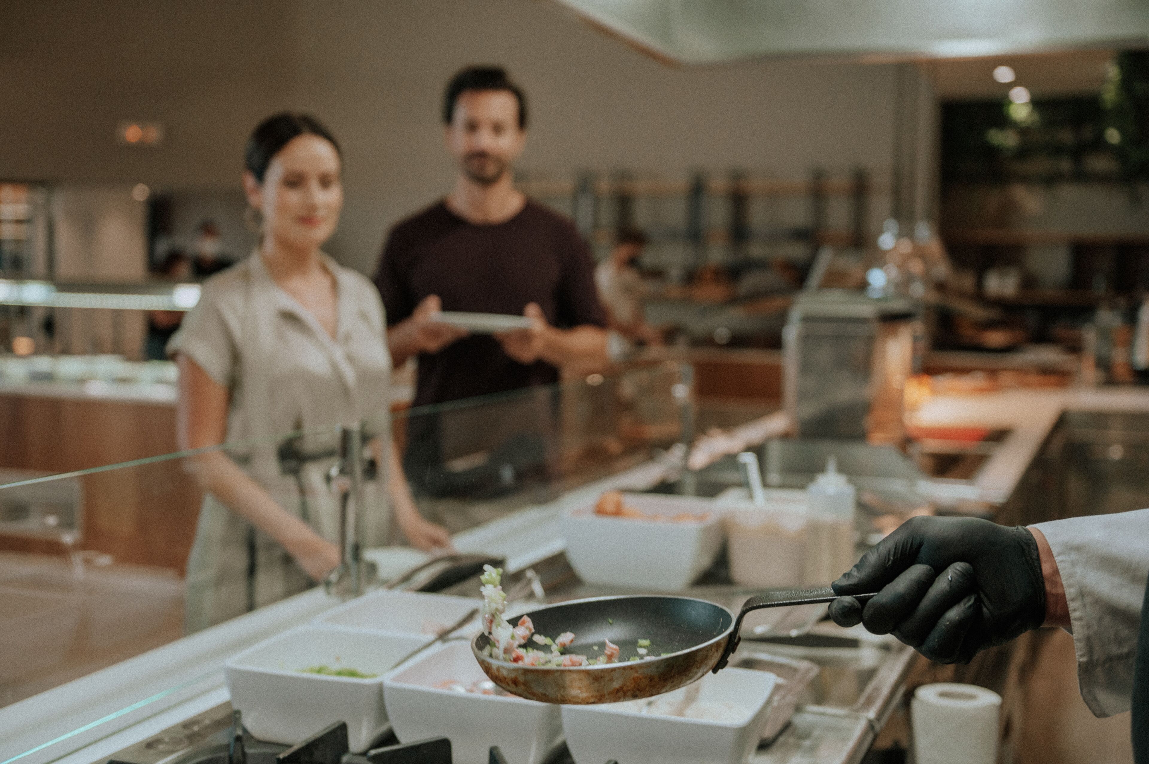 A person serving food in a modern restaurant setting with a clear view of the counter and various food containers.