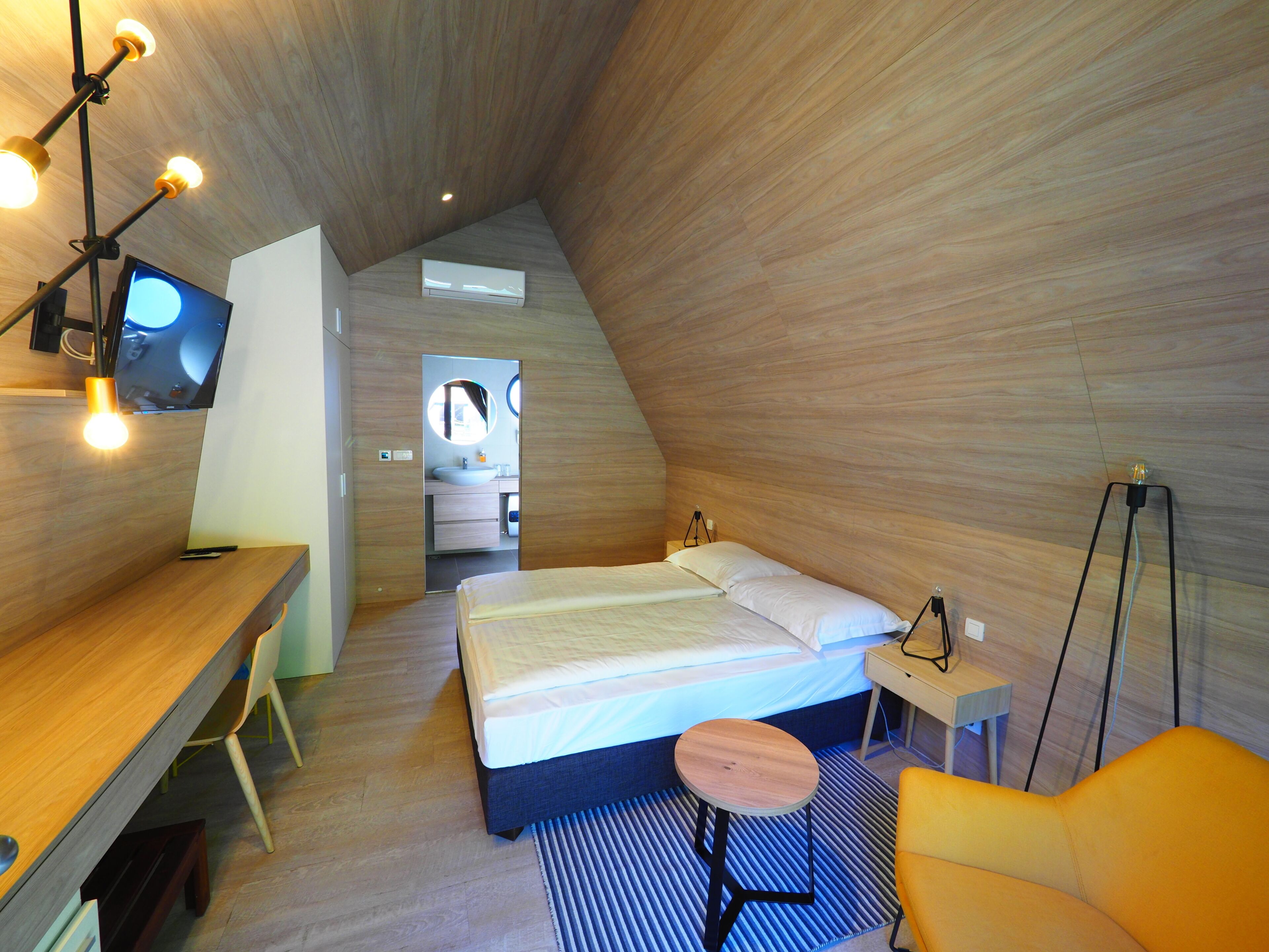 A modern, compact bedroom with a bed, bedside table, and a desk area.