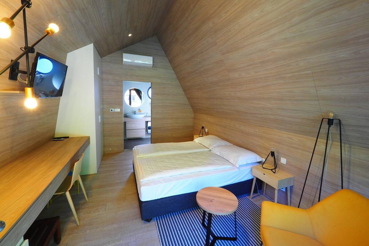 A modern, compact bedroom with a bed, bedside table, and a desk area.