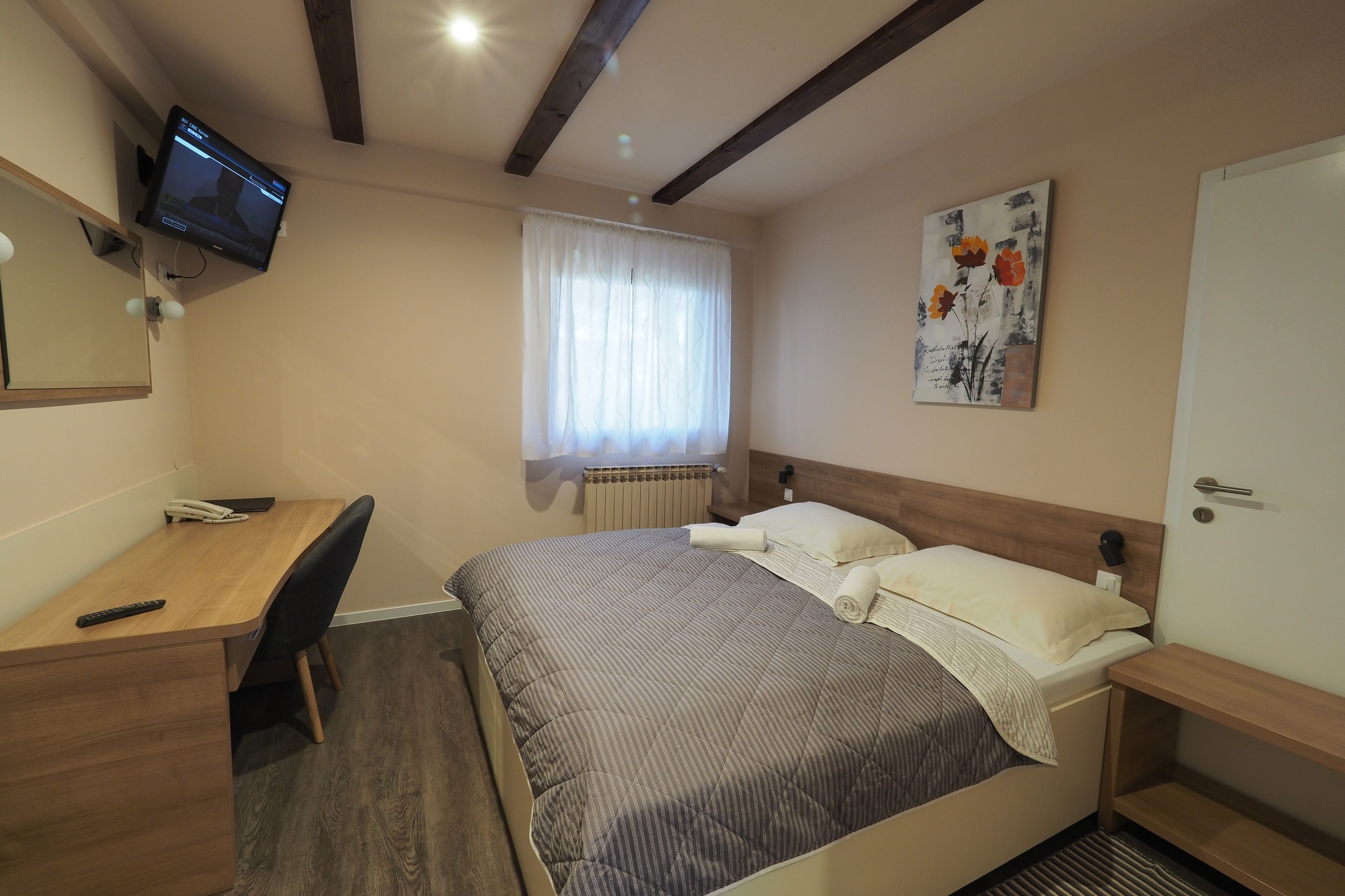 A bedroom with a bed, a desk, a chair, a television mounted on the wall, and a window with curtains.