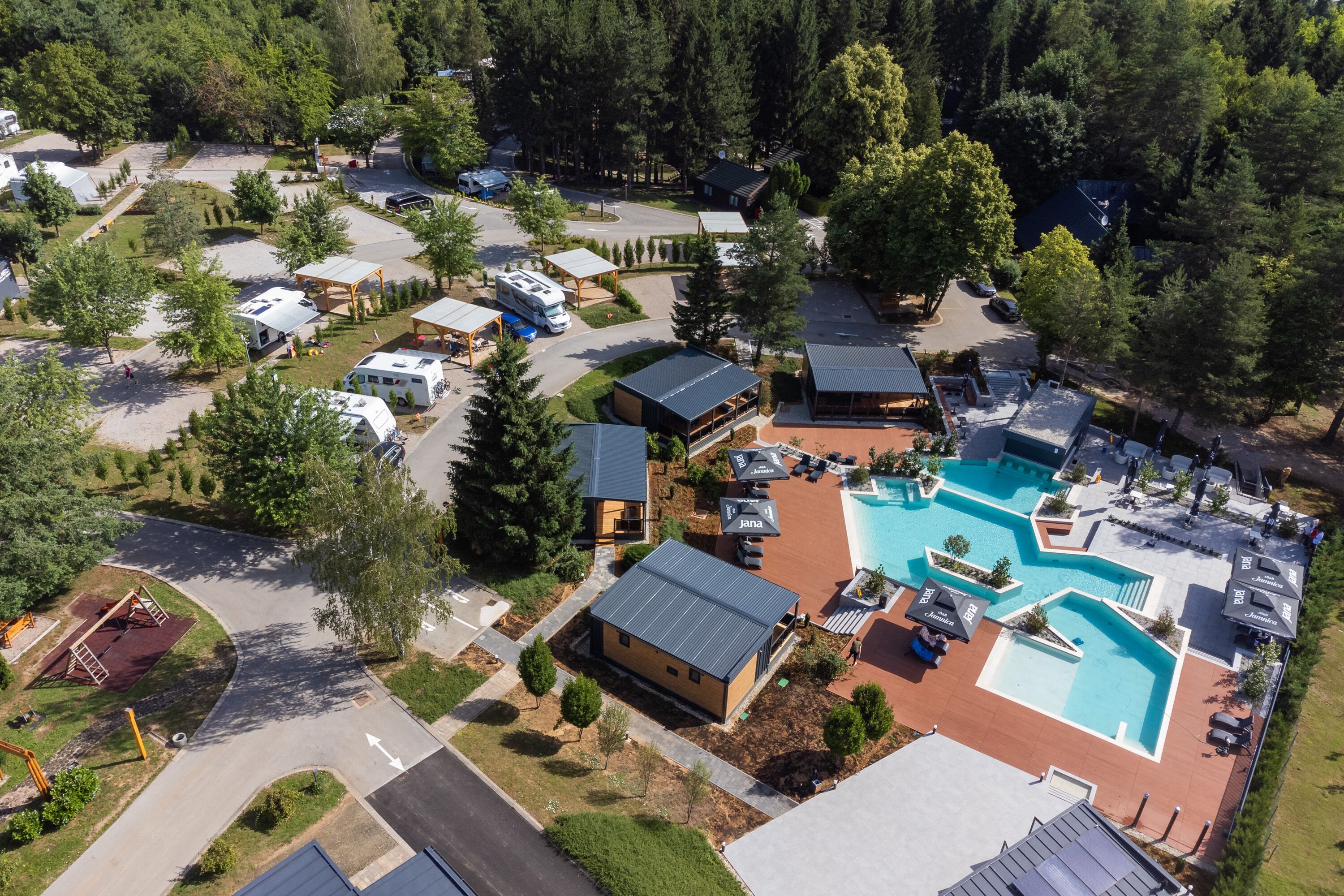 An aerial view of a campground with RVs, a swimming pool, and various buildings.