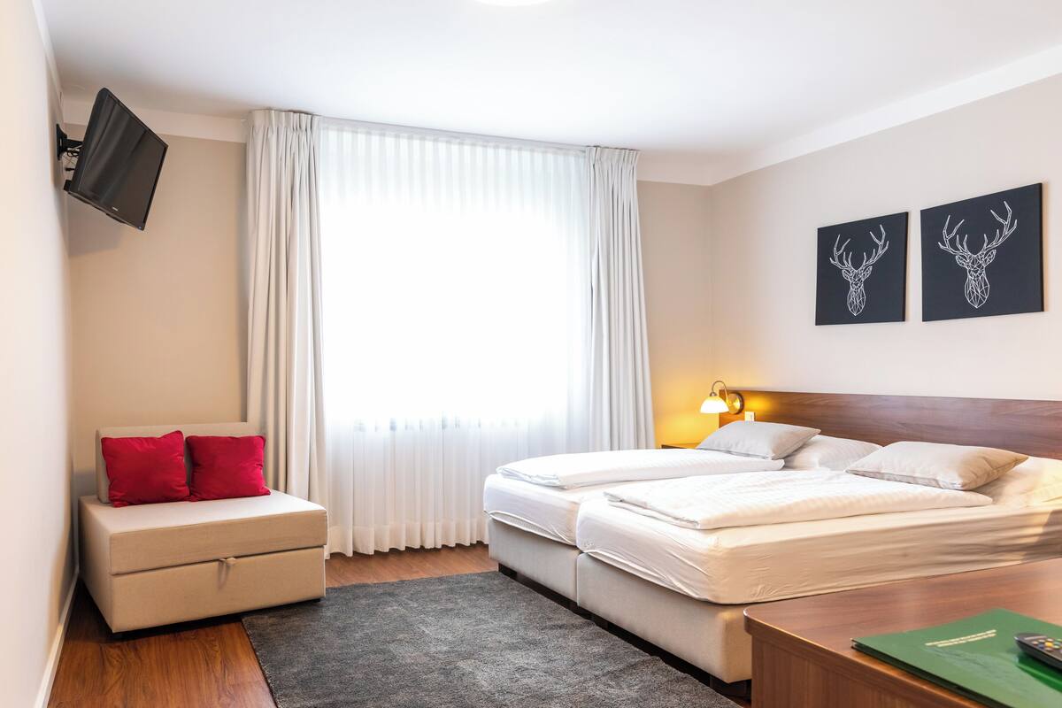 A hotel room with a bed, a desk, a TV mounted on the wall, and two artwork pieces on the wall.