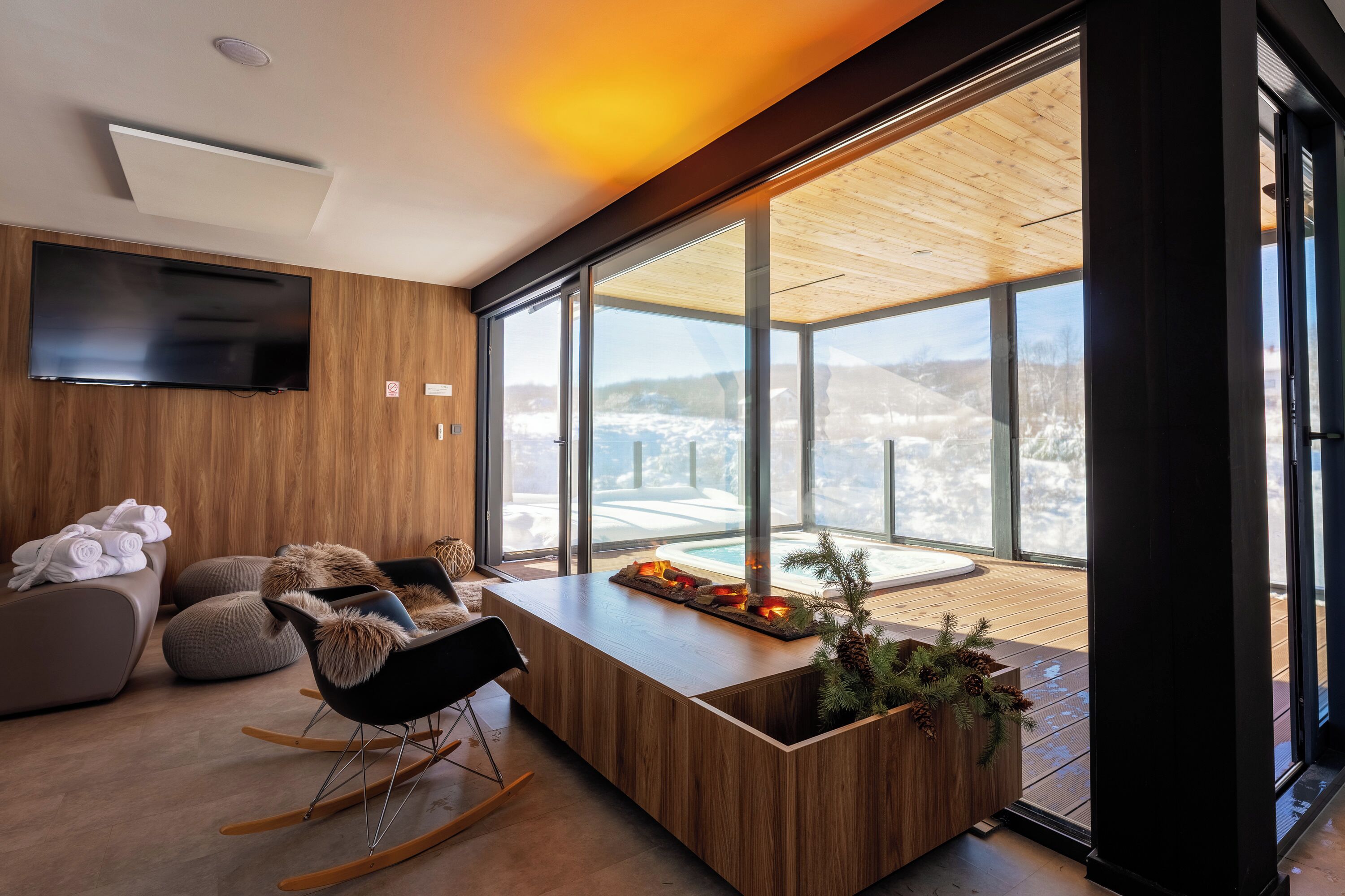 Una sala de estar moderna con techo de madera, ventanas amplias, un televisor de pantalla plana, una mesa de centro de madera y un rincón de descanso acogedor.