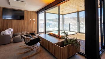 Una sala de estar moderna con techo de madera, ventanas amplias, un televisor de pantalla plana, una mesa de centro de madera y un rincón de descanso acogedor.