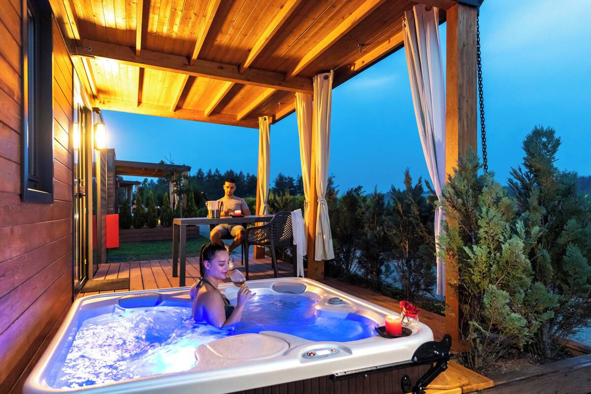 A hot tub with a wooden deck and a view of trees.
