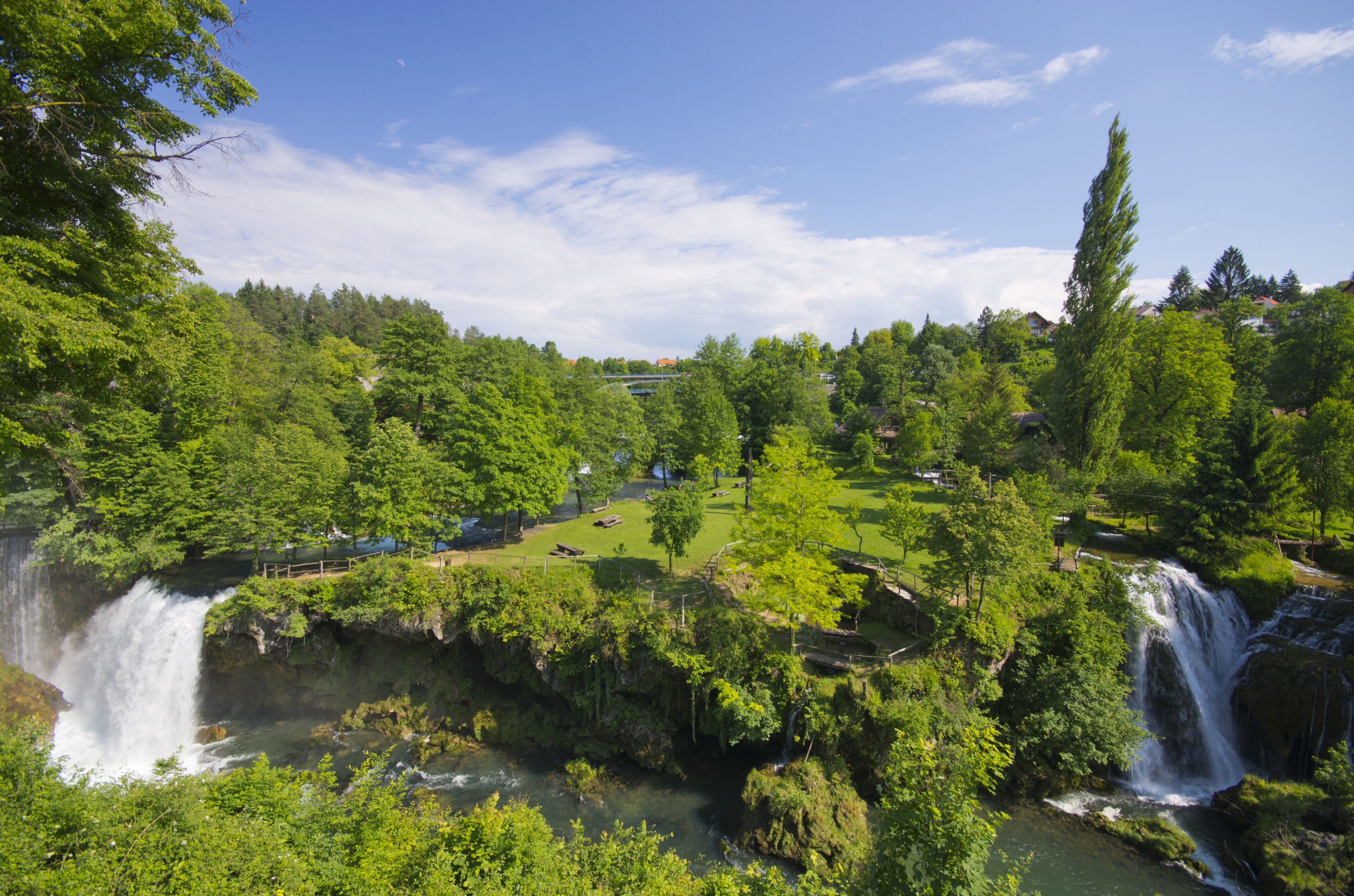 Una cascada envoltada de vegetació exuberant sota un cel blau clar.