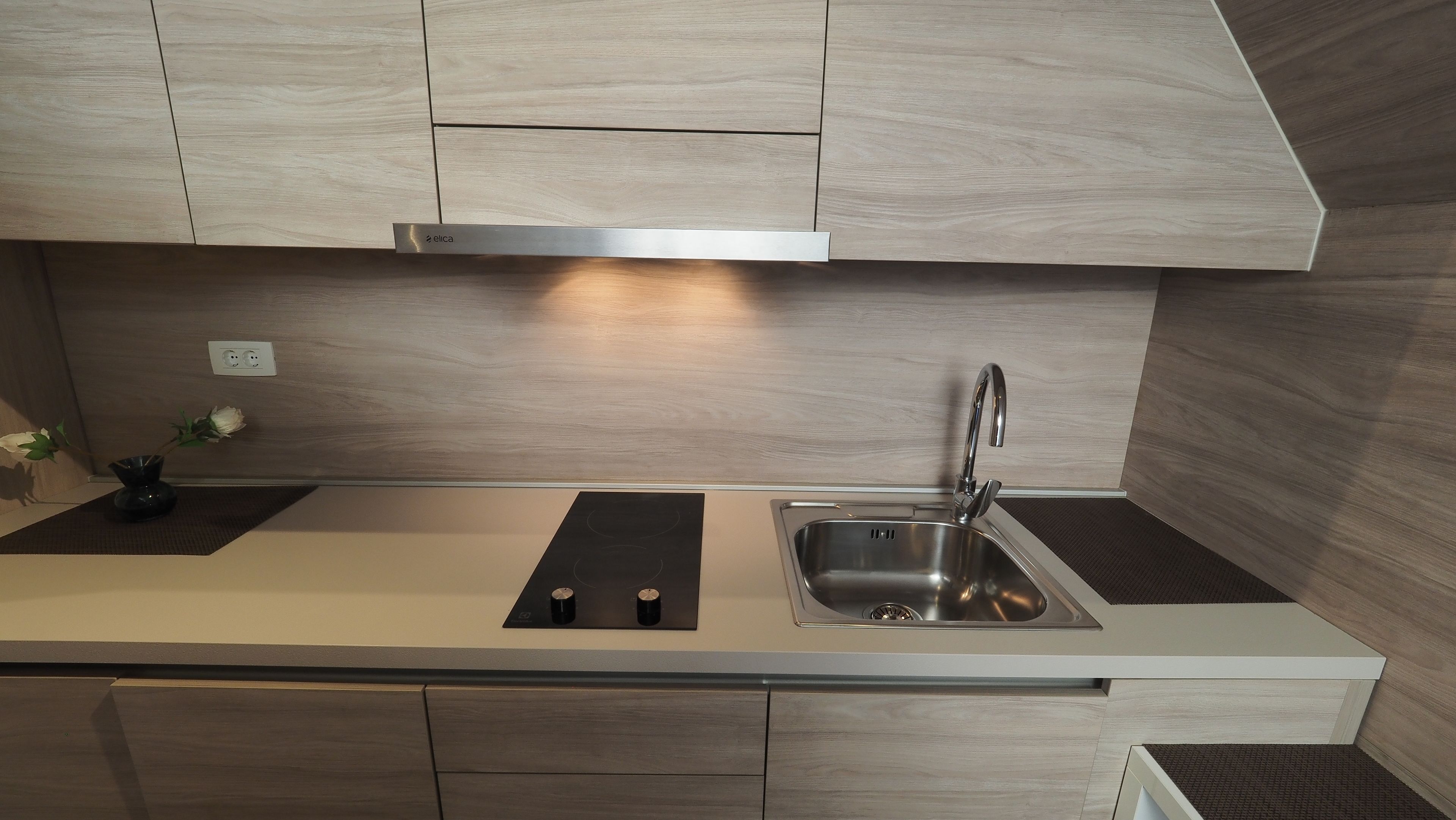 Una cocina moderna con un lavamanos de acero inoxidable, una placa de inducción negra y armarios de madera.