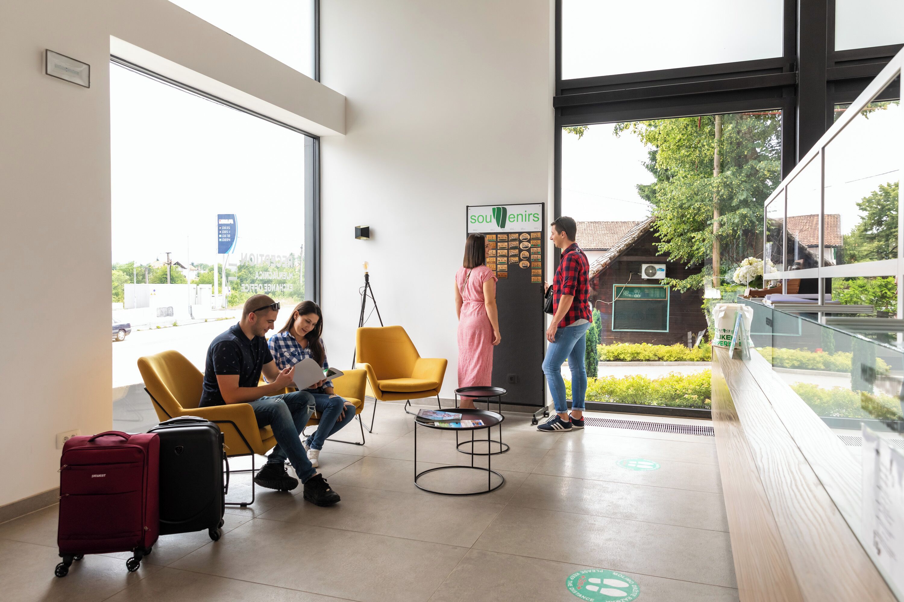 Een wachtruimte met gele stoelen, een receptiebalie en uitzicht op buiten.