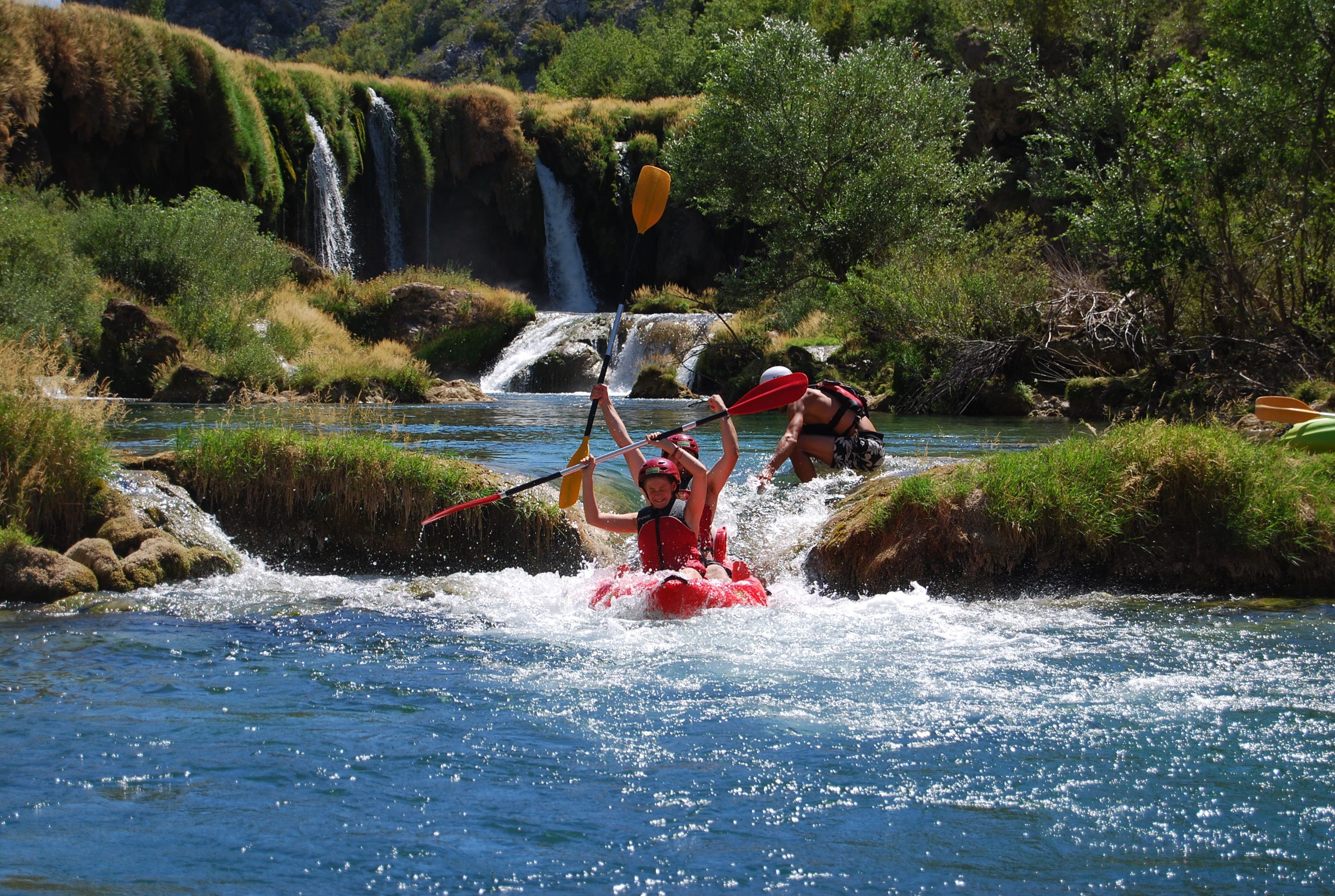 Una persona practica kayak en un río rodeado de vegetación y cascadas.