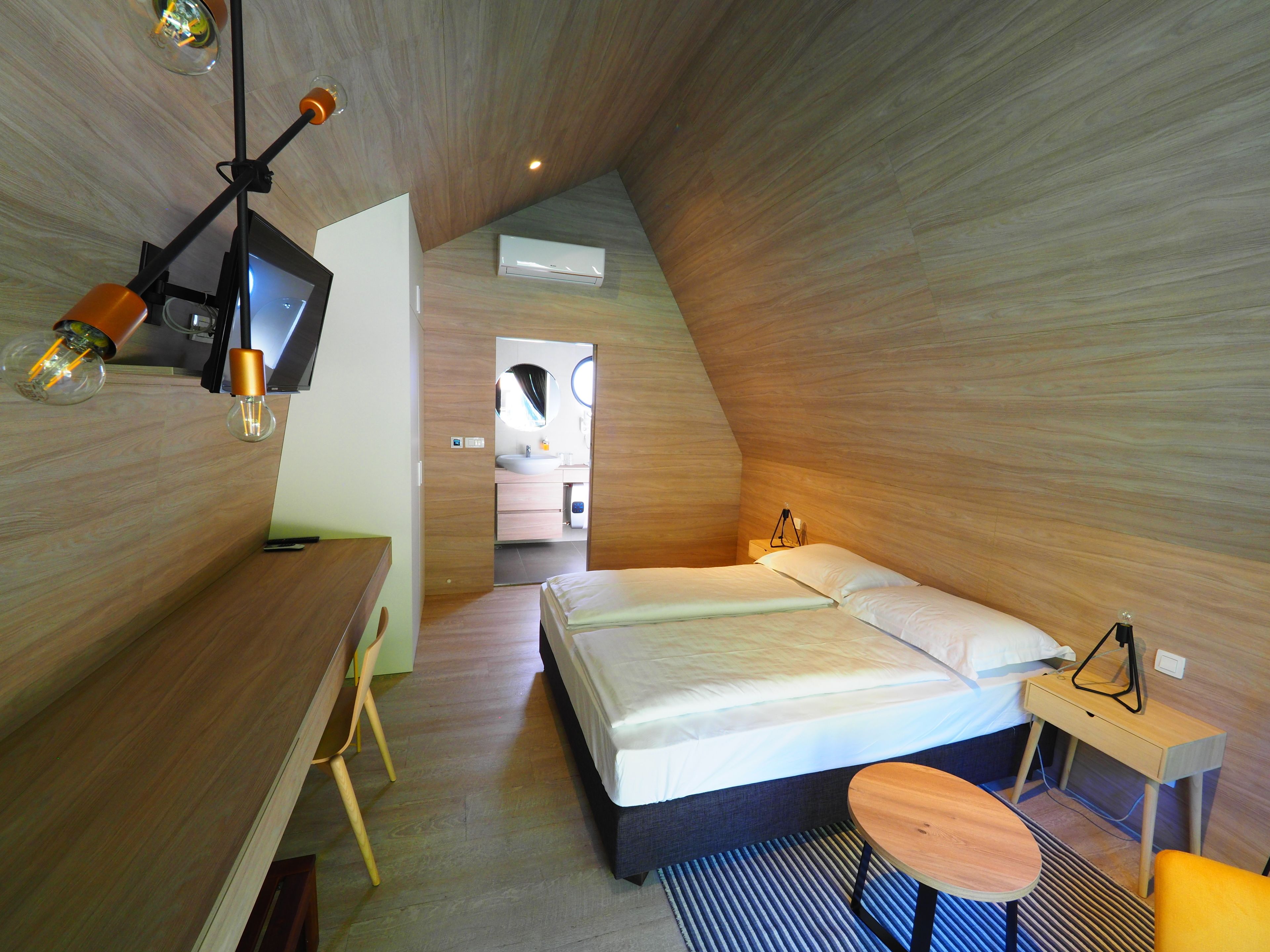 A modern, compact bedroom with a bed, bedside table, and a desk area.