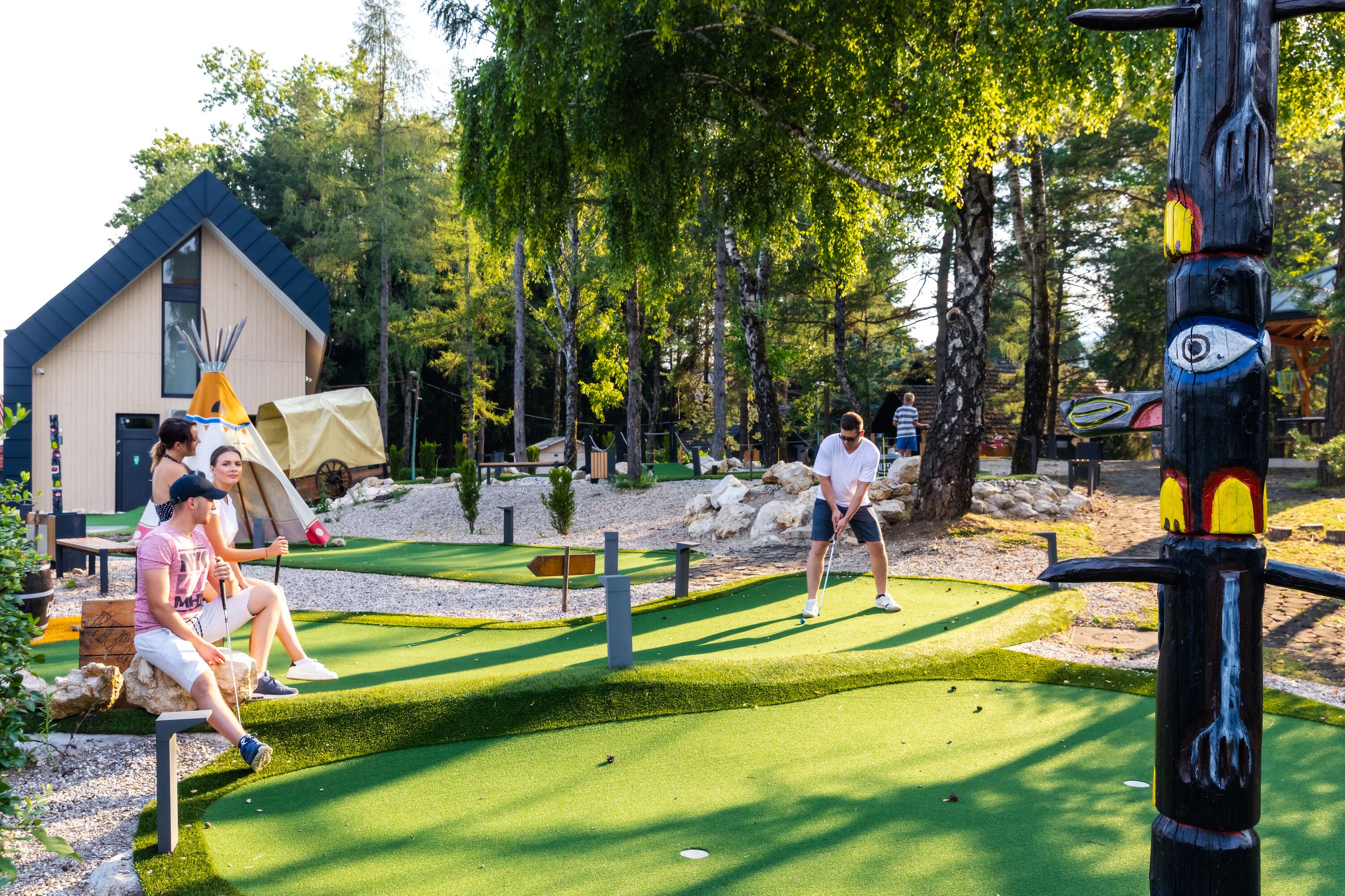 Un campo da golf con un tee, un putting green e un edificio in legno sullo sfondo.