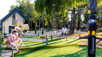 Un campo da golf con un tee, un putting green e un edificio in legno sullo sfondo.