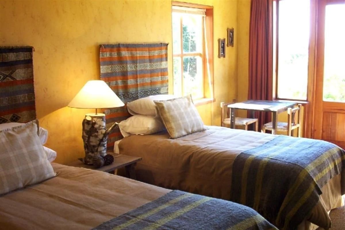 A room with two beds, a table, a lamp, and a window with curtains.
