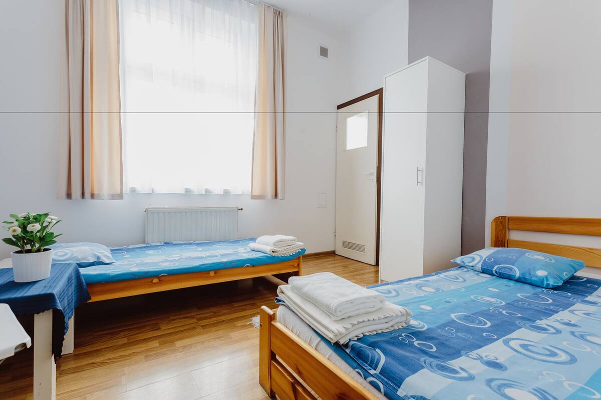 Ein Schlafzimmer mit zwei Einzelbetten, einem Holzkopfteil, einem Heizkörper, einem Kleiderschrank und einem Fenster mit Vorhängen.