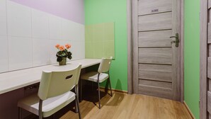Une petite pièce avec une table blanche, deux chaises blanches, une plante en pot et une porte en bois avec une plaque numérotée.