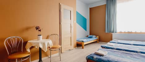 A room with a bed, a chair, a small table with a vase, and a window with curtains.