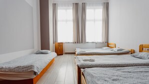 Une pièce avec trois lits en bois alignés contre un mur, un radiateur et une fenêtre avec des rideaux.