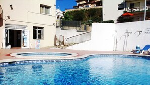 Uma piscina com borda azulejada, um edifício com fachada branca e um guarda-sol vermelho.