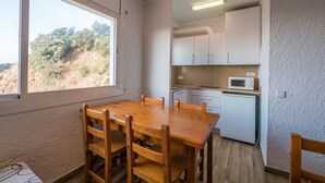 Cozinha compacta com armários brancos, micro-ondas e janela com vista para uma colina.