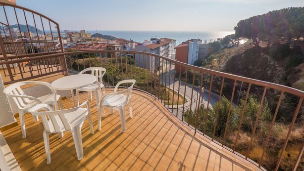 Varanda com vista para o mar, cadeiras de plástico branco e uma mesa.