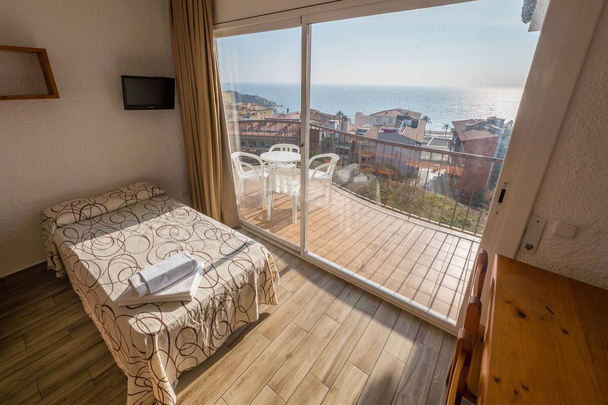 A bedroom with a large balcony, a bed with a patterned bedspread, and a TV mounted on the wall.