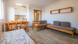Quarto compacto com cama, sofá, mesa de jantar com cadeiras, cozinha compacta e quadro com moldura de madeira na parede.