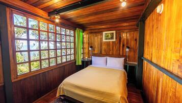 A wooden-paneled room with a bed, large windows, and a view of trees.