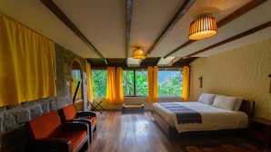 Una habitación con cama, sofá y una mesita. Hay cortinas y una ventana con vistas a zonas verdes.