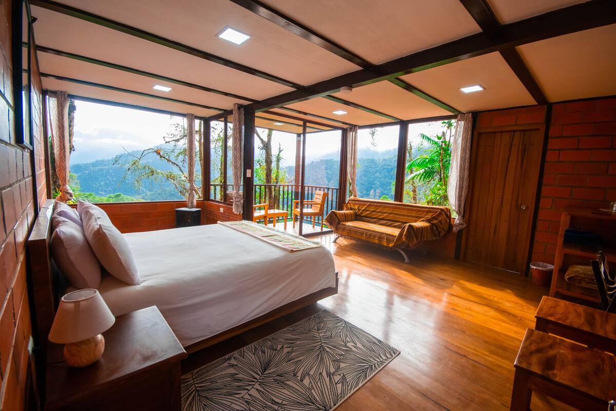 Un dormitorio amplio con una cama grande, un banco de madera y vistas a exuberante vegetación.