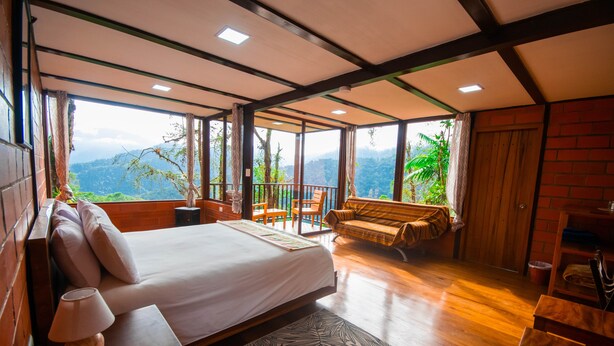 Un dormitorio amplio con una cama grande, un banco de madera y vistas a exuberante vegetación.