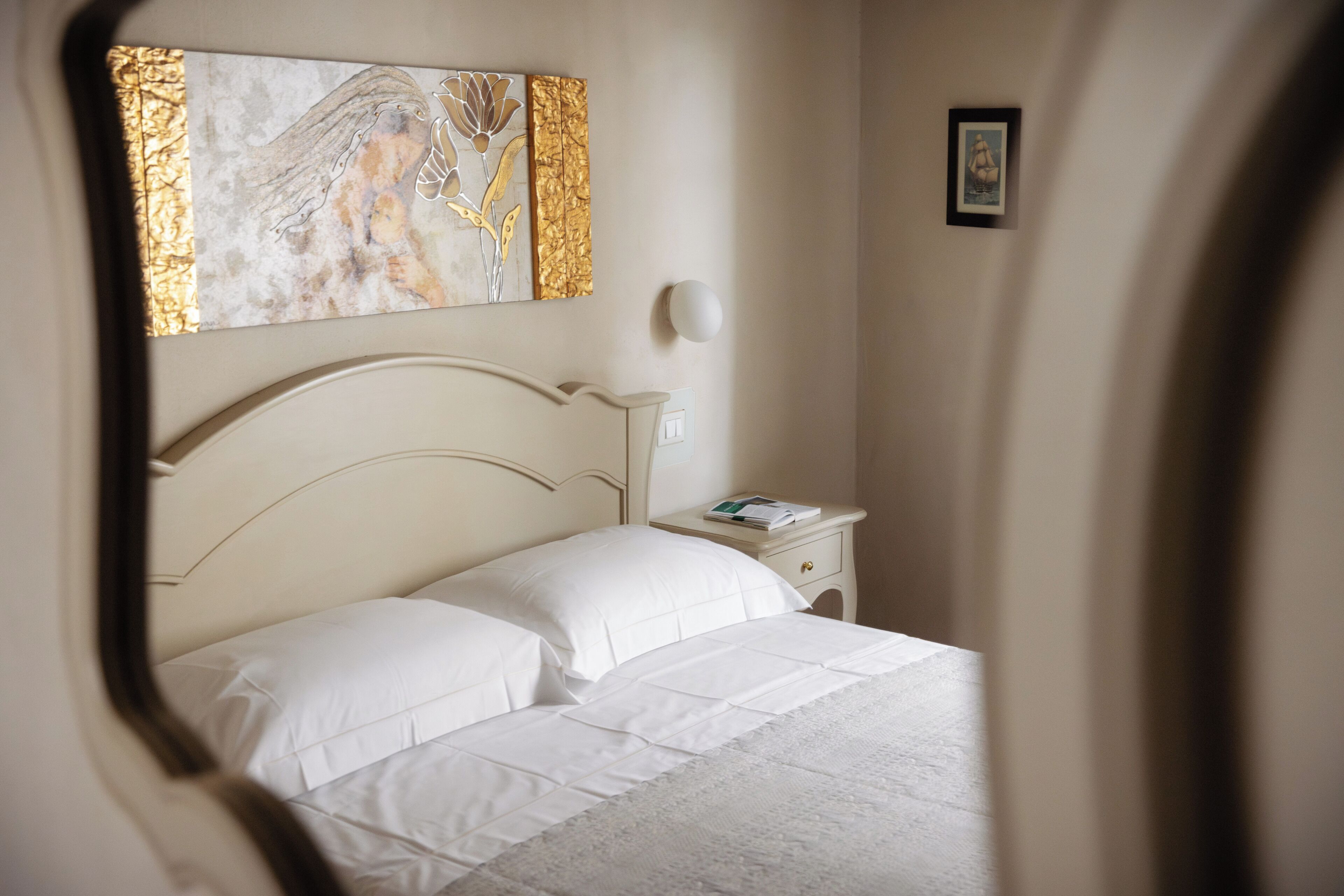 A neatly made bed with white linens, a bedside table with a book, and a wall-mounted light fixture.