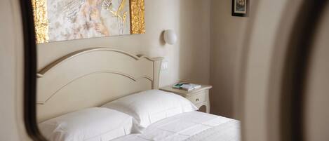 A neatly made bed with white linens, a bedside table with a book, and a wall-mounted light fixture.
