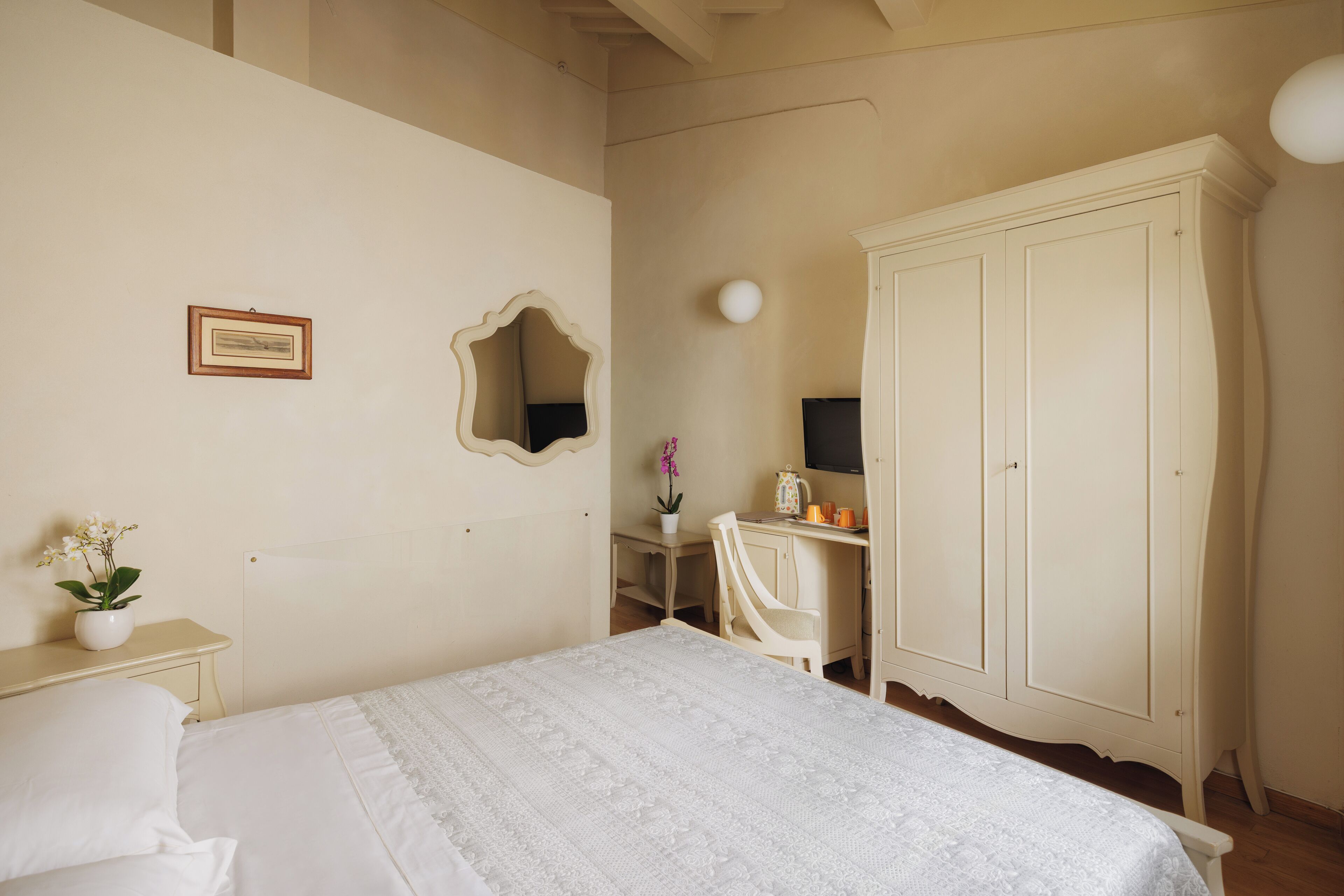 A bedroom with a bed, a desk, a chair, a wardrobe, and a mirror on the wall.