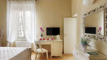 Une chambre à coucher comprenant un lit, un bureau, une chaise, une commode, un miroir et une fenêtre avec des rideaux légers.
