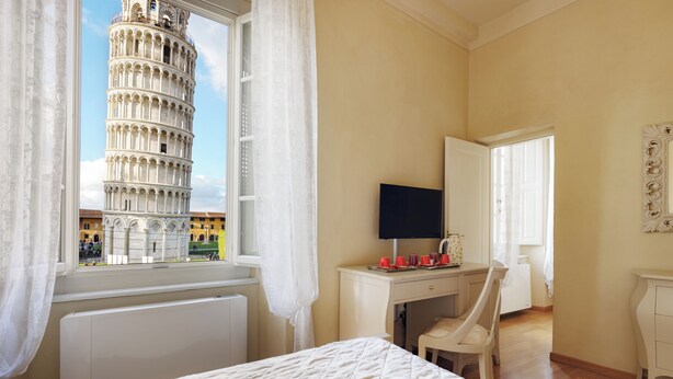 A bedroom with a bed, a desk, a chair, and a window with a view of the Leaning Tower of Pisa. - Residenza d'Epoca Relais I Miracoli (Pisa)