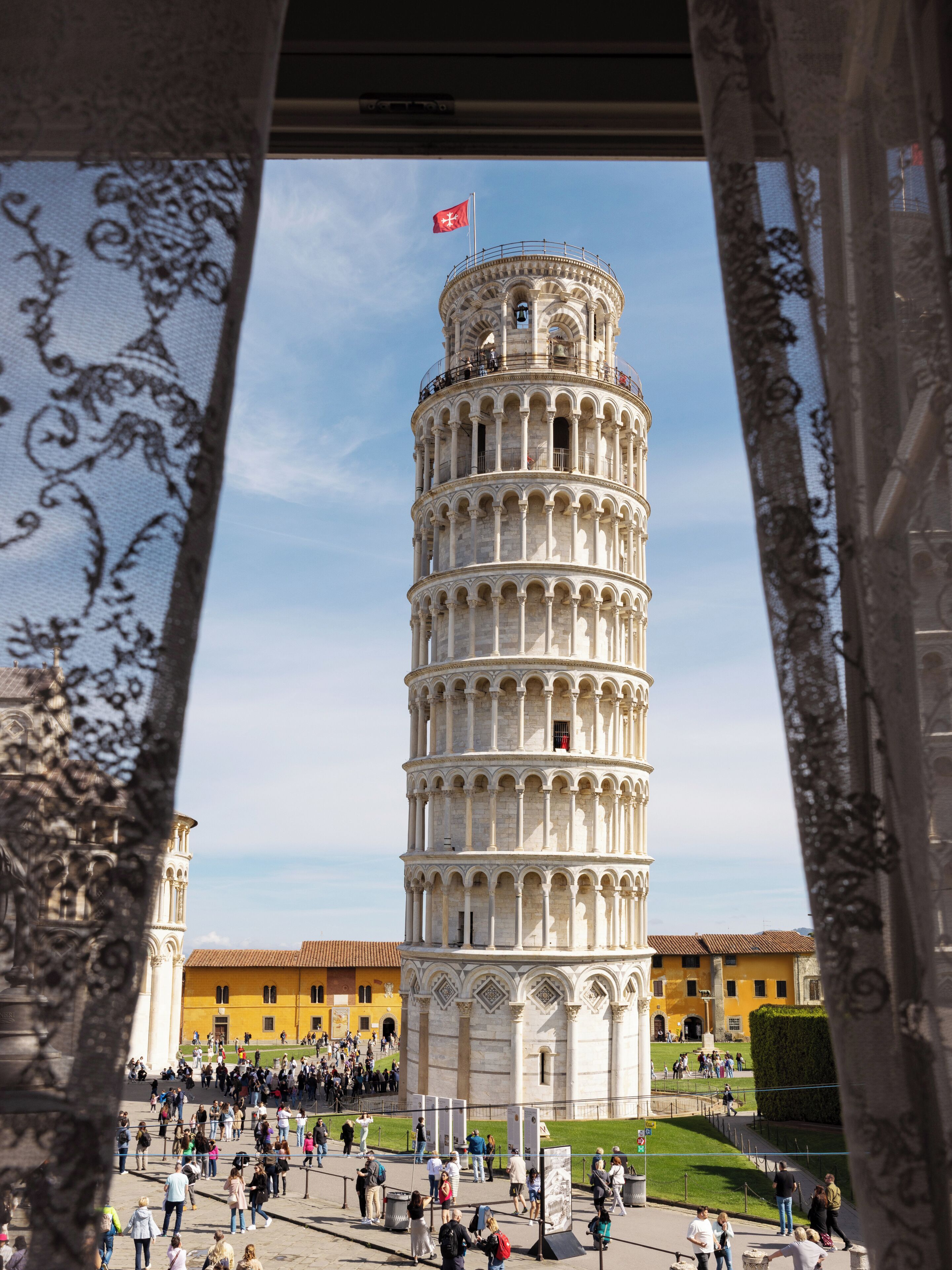Una torre histórica de varios niveles, rodeada por una plaza con gente y edificios.
