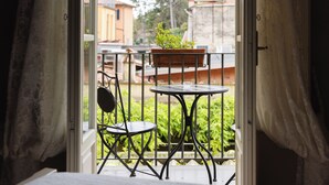 A balcony with a table and chair, a potted plant, and a view of buildings and trees. - Residenza d'Epoca Relais I Miracoli (Pisa)