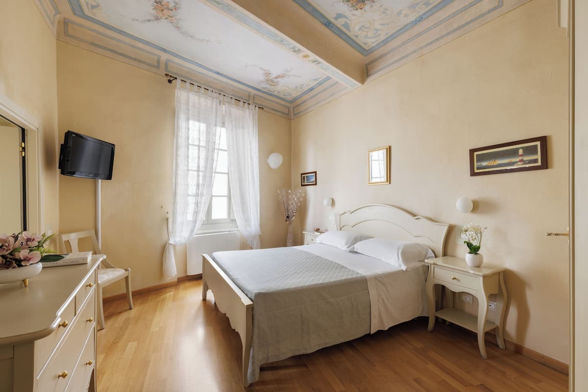 A bedroom with a bed, bedside tables, a dresser, a television, and a window with curtains.