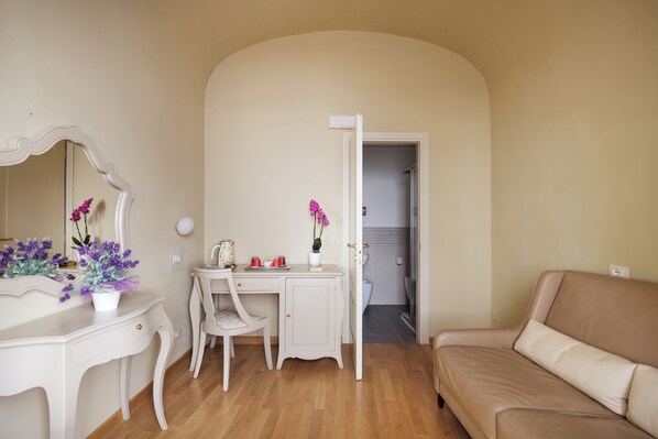 A room with a white vanity, a beige sofa, and a desk with a chair.