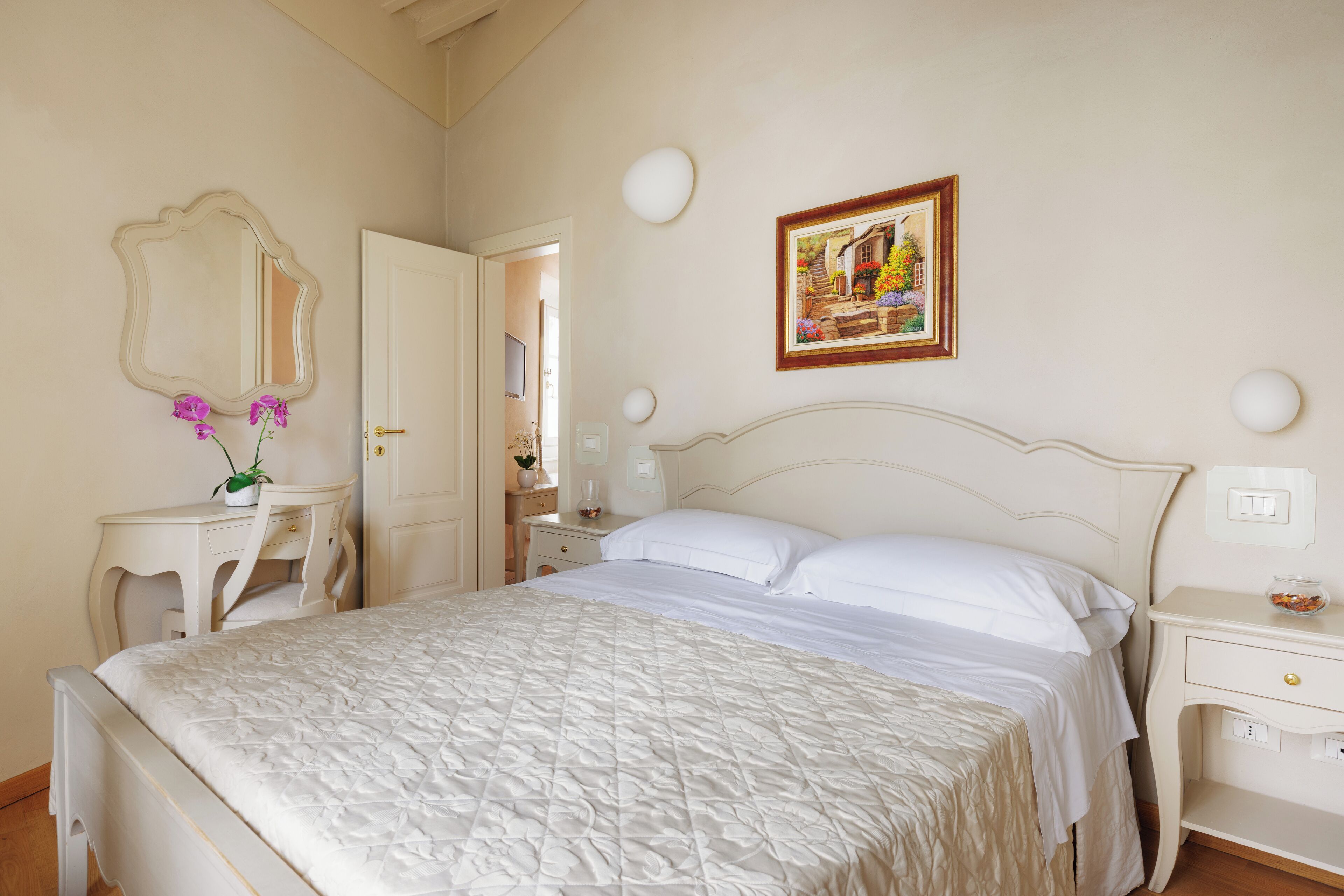 Une chambre à coucher comprenant un lit, une table de chevet, une commode, un miroir et un tableau accroché au mur.