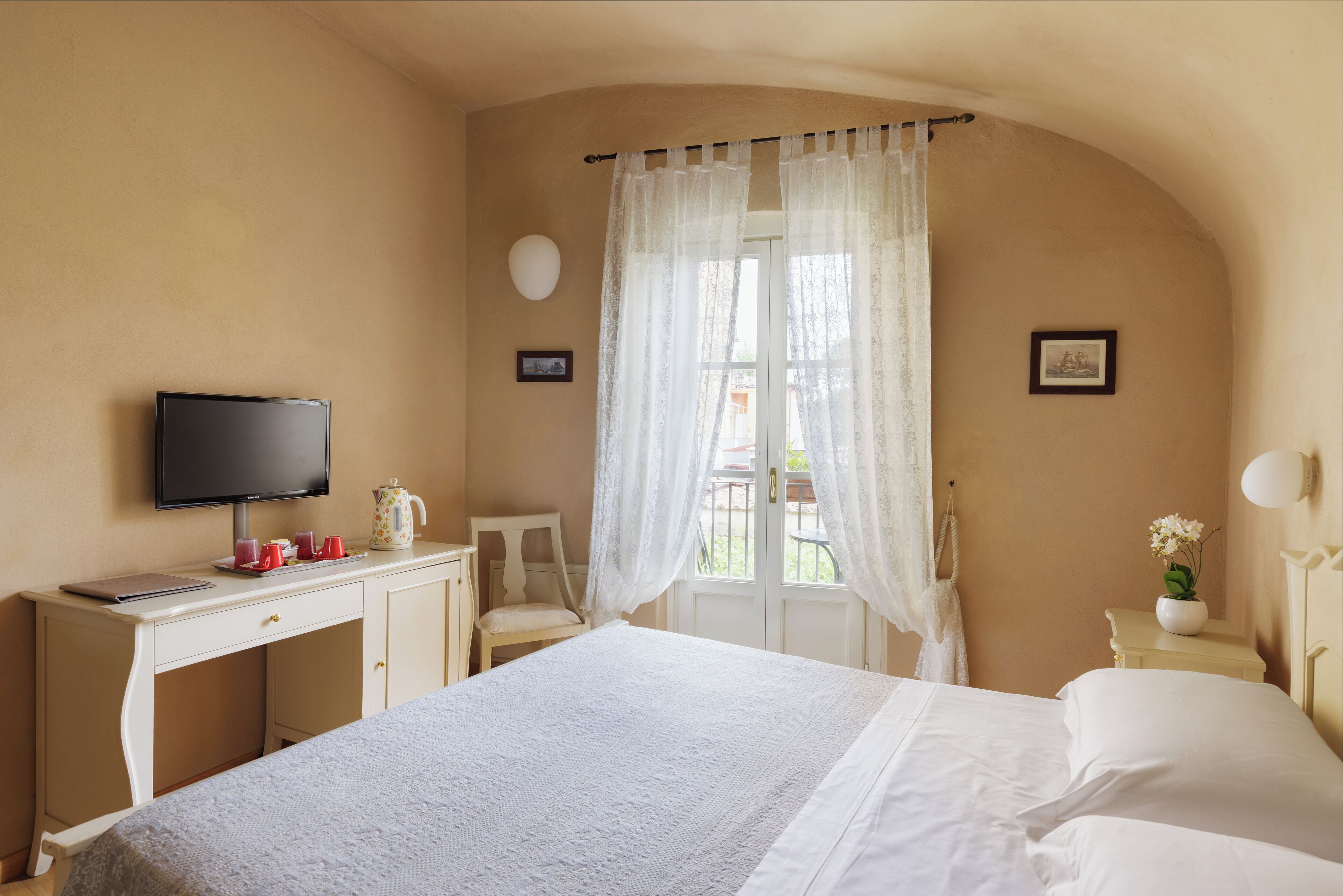 Una camera d'albergo con un letto, una scrivania con un portatile, una televisione e una finestra con tende.