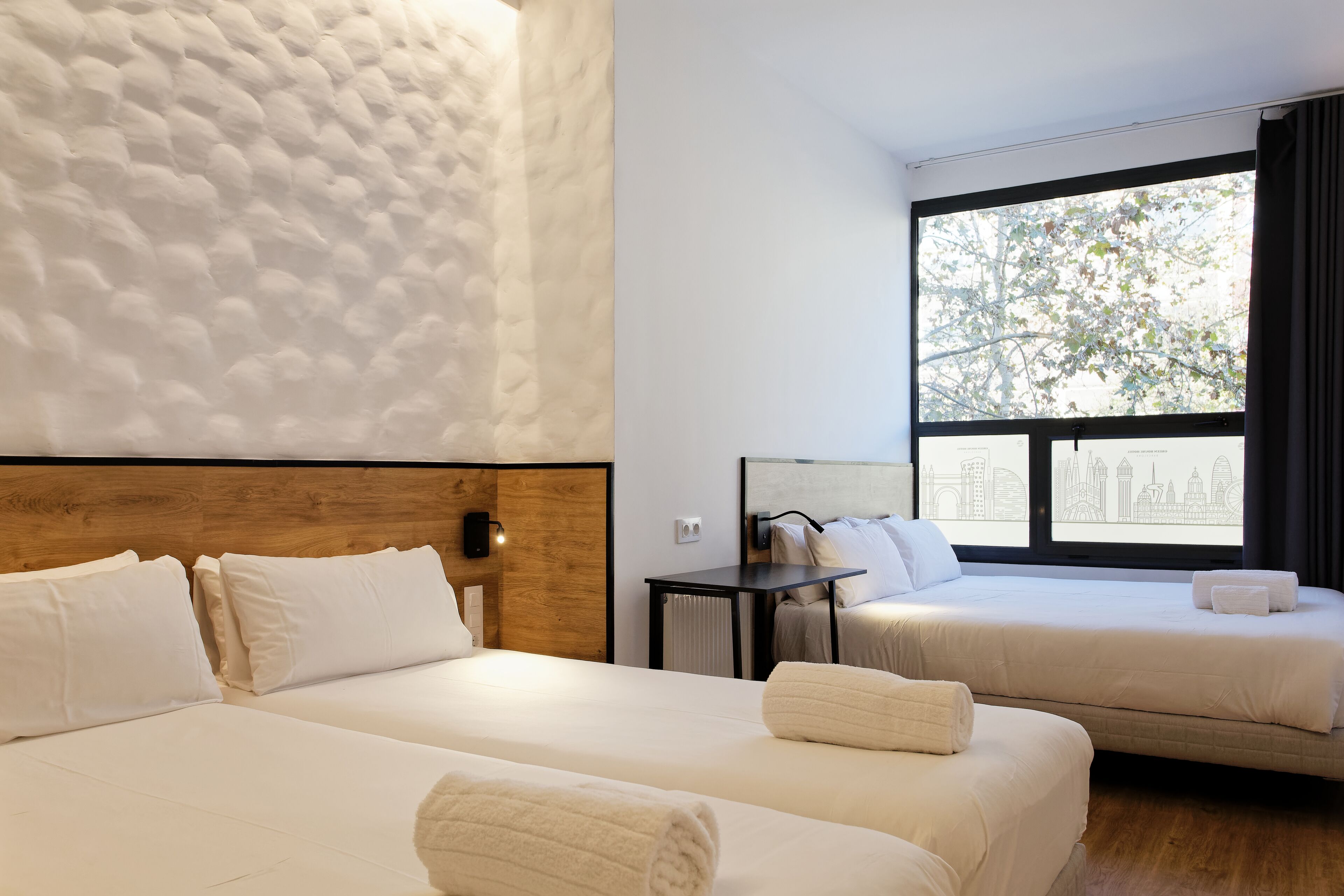Hotelkamer met twee bedden, een houten hoofdbord, een nachtkastje, een raam met uitzicht op de stad en een structuurwand.