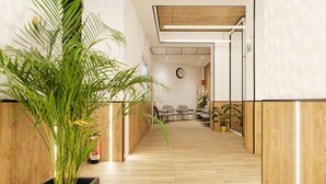 A modern hallway with wooden flooring, a large potted plant, and a reception area with chairs and a clock. -  Green House Hotel (Barcelona)