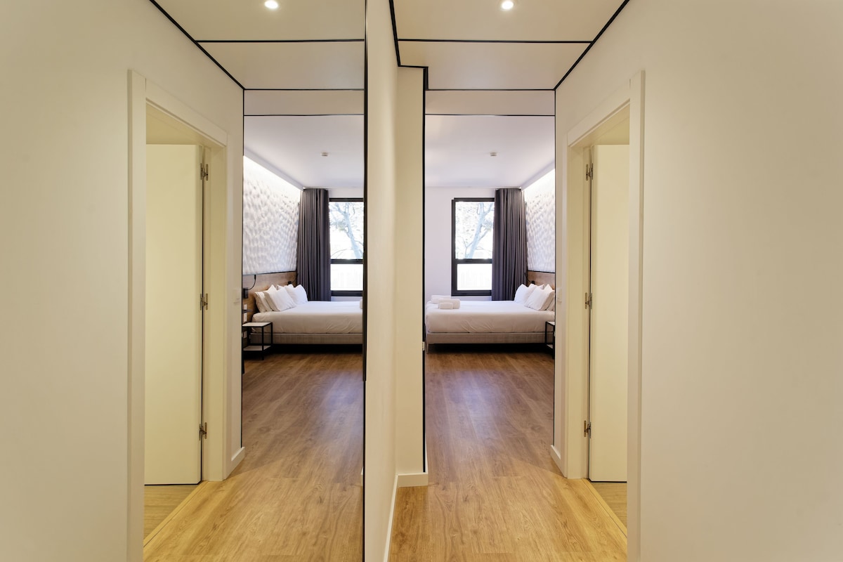 A mirrored hallway leading to a bedroom with a bed, nightstands, and a window with curtains.