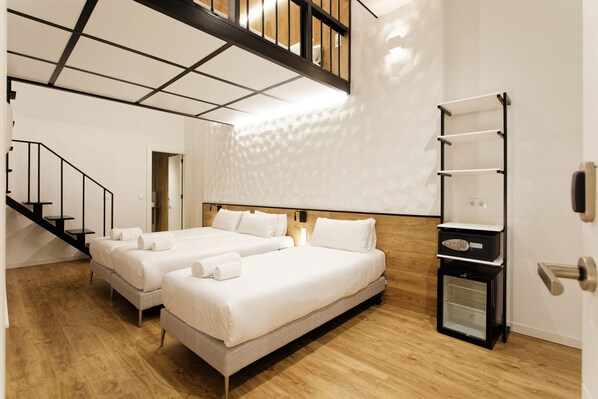 Quarto de hotel com duas camas, aquecedor embutido, piso de madeira e uma escada.