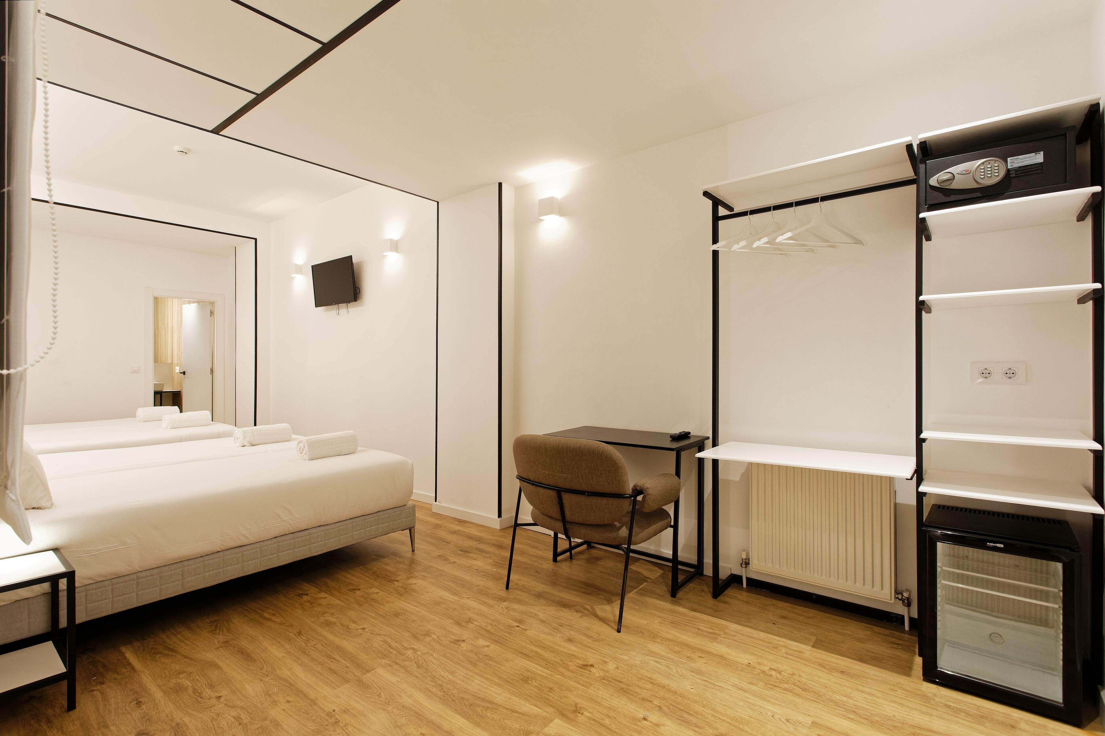 Ein Hotelzimmer mit Bett, Schreibtisch, Stuhl, Heizkörper und einer Minibar.