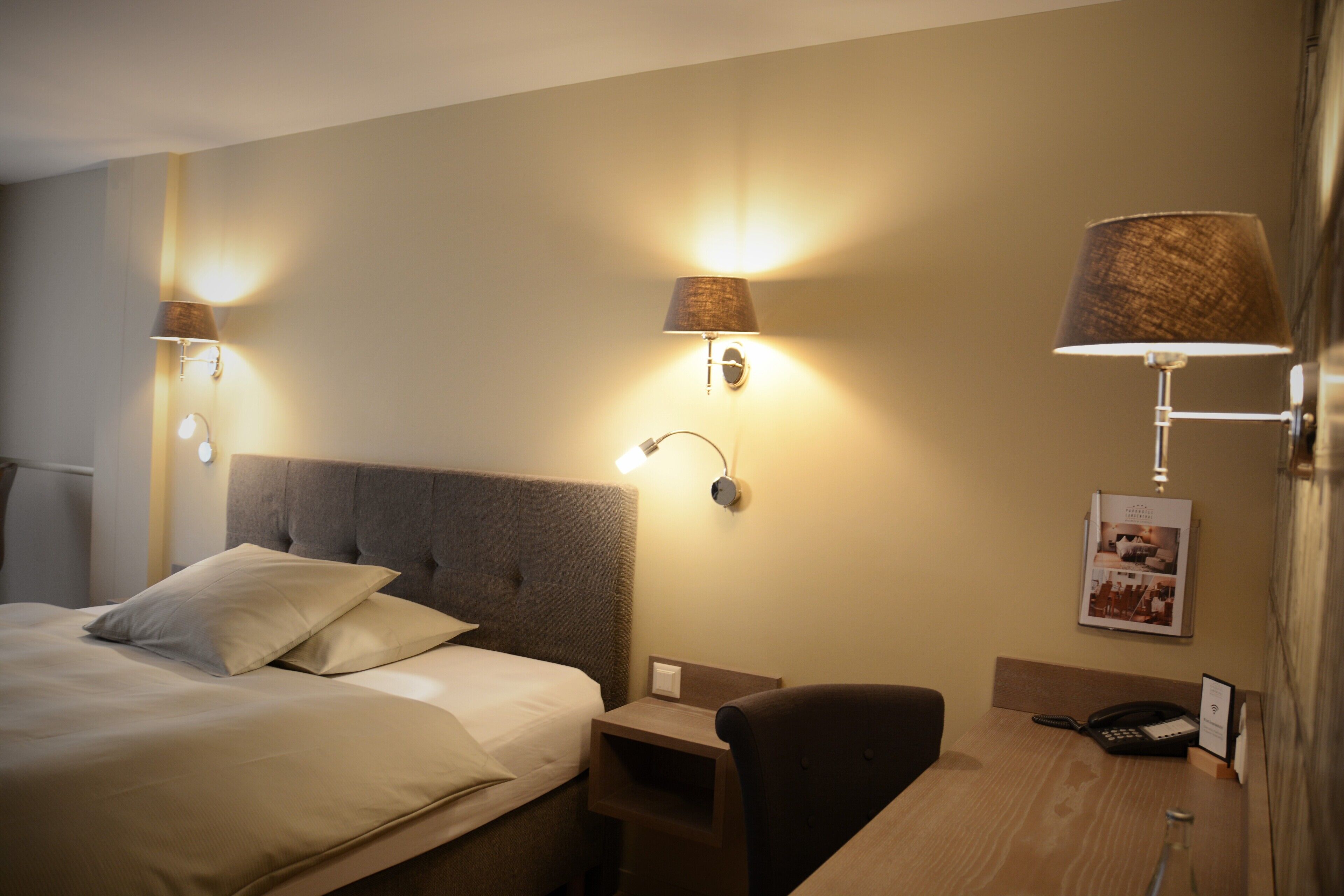 Ein Hotelzimmer mit einem großen Bett, Nachttischlampen, einem Schreibtisch mit Stuhl und einem Telefon.