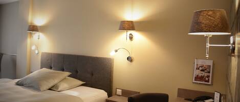 A hotel room with a large bed, bedside lamps, a desk with a chair, and a telephone.