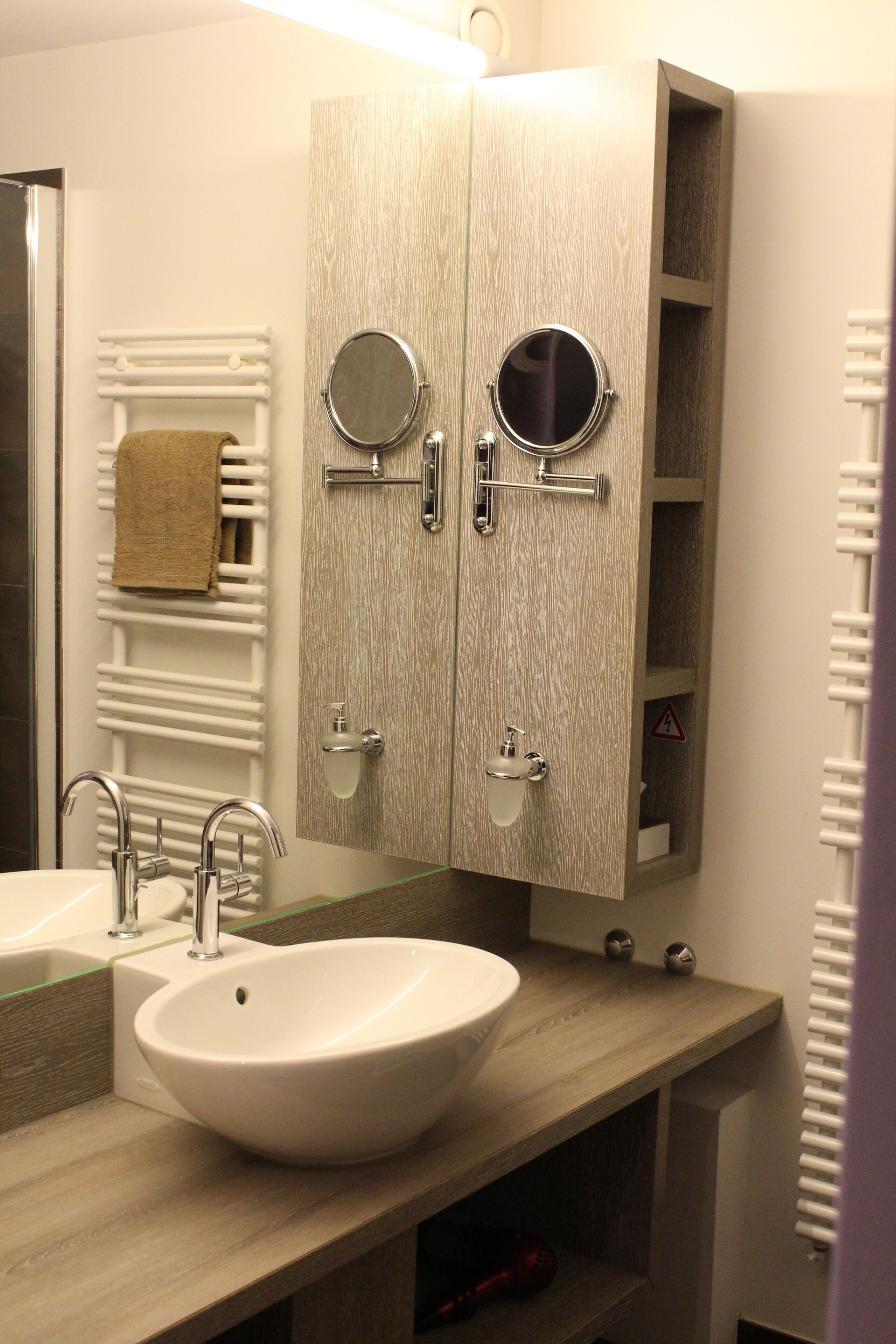 A bathroom with a large sink, two mirrors, a towel rack, and a cabinet with shelves.