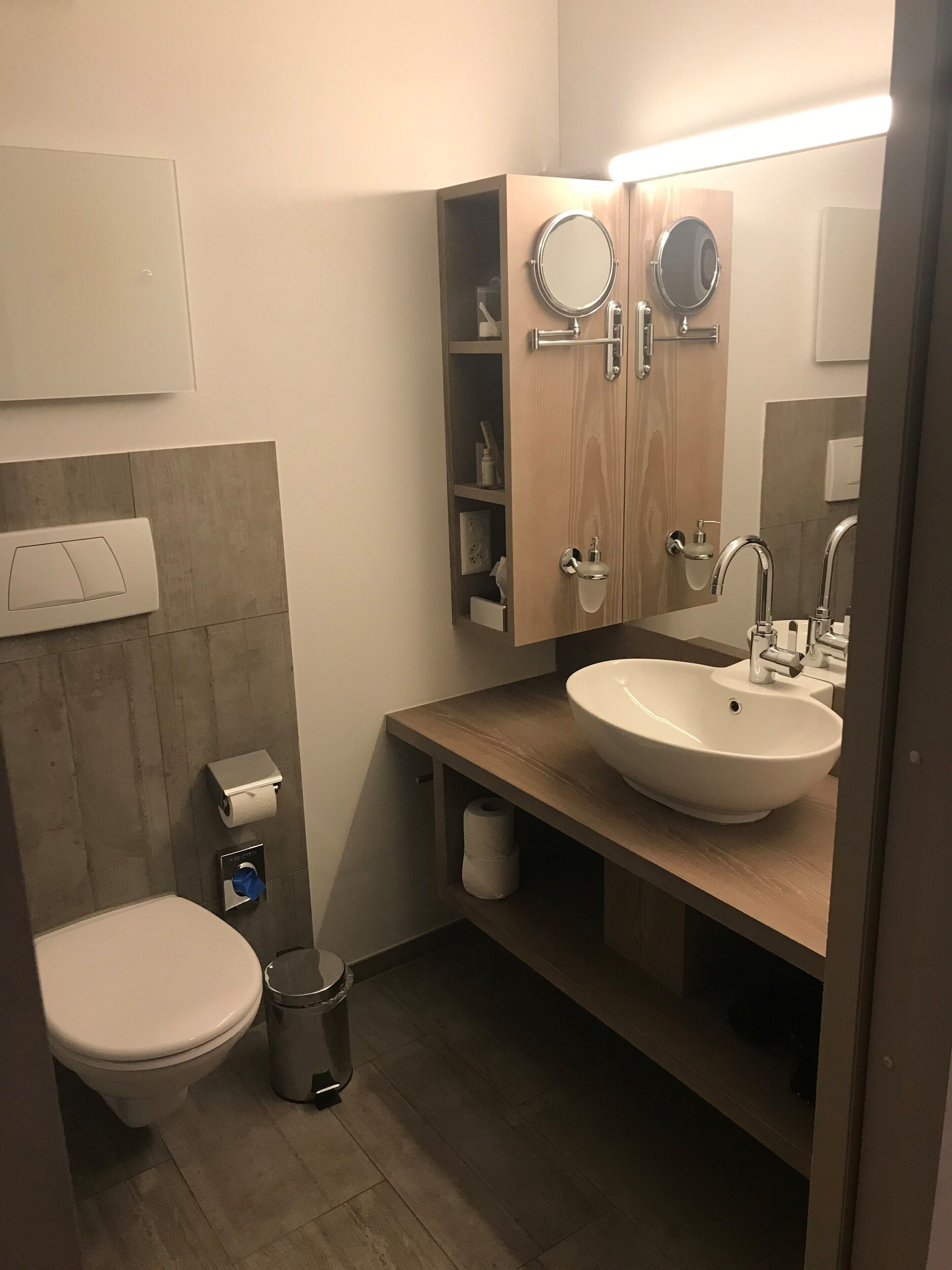 A modern bathroom with a toilet, bidet, sink, and mirror.